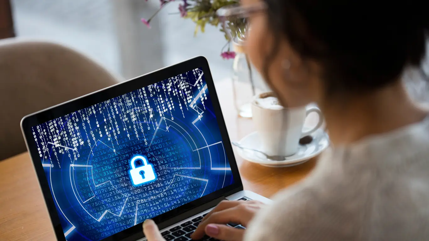 Person working on laptop with digital lock icon on screen representing steps to improve cybersecurity compliance processes